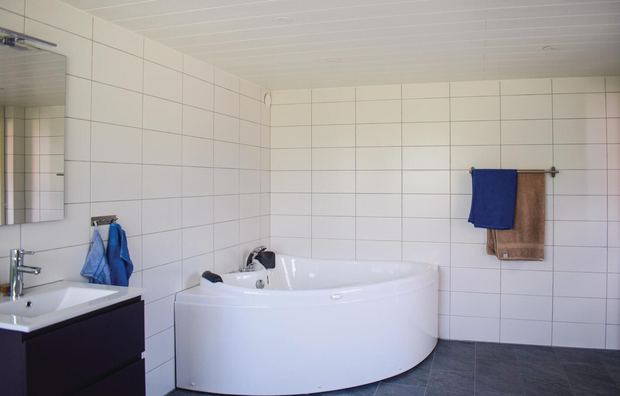 Une salle de bain moderne avec une grande baignoire, un meuble-lavabo avec un miroir et un porte-serviettes avec deux serviettes.