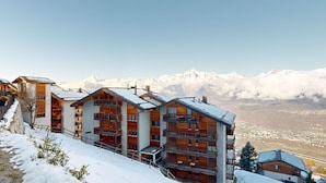 Eine Reihe von Holzhütten mit Balkonen vor der Kulisse von schneebedeckten Bergen und einem klaren Himmel.
