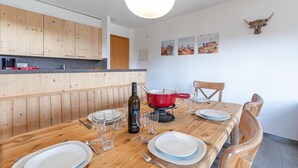 A wooden dining table set with plates, glasses, and cutlery, a red pot on a stove, and a bottle of wine. - Mélèzes R 020 - SKI LIFT apartment 8 people (Veysonnaz)