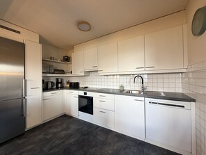 A modern kitchen with white cabinets, a stainless steel refrigerator, a dishwasher, and a built-in oven.