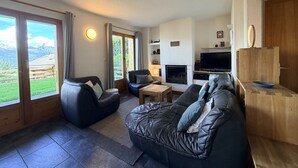 Un salon doté d’une cheminée, d’un téléviseur et offrant une vue sur les montagnes grâce à de grandes fenêtres.