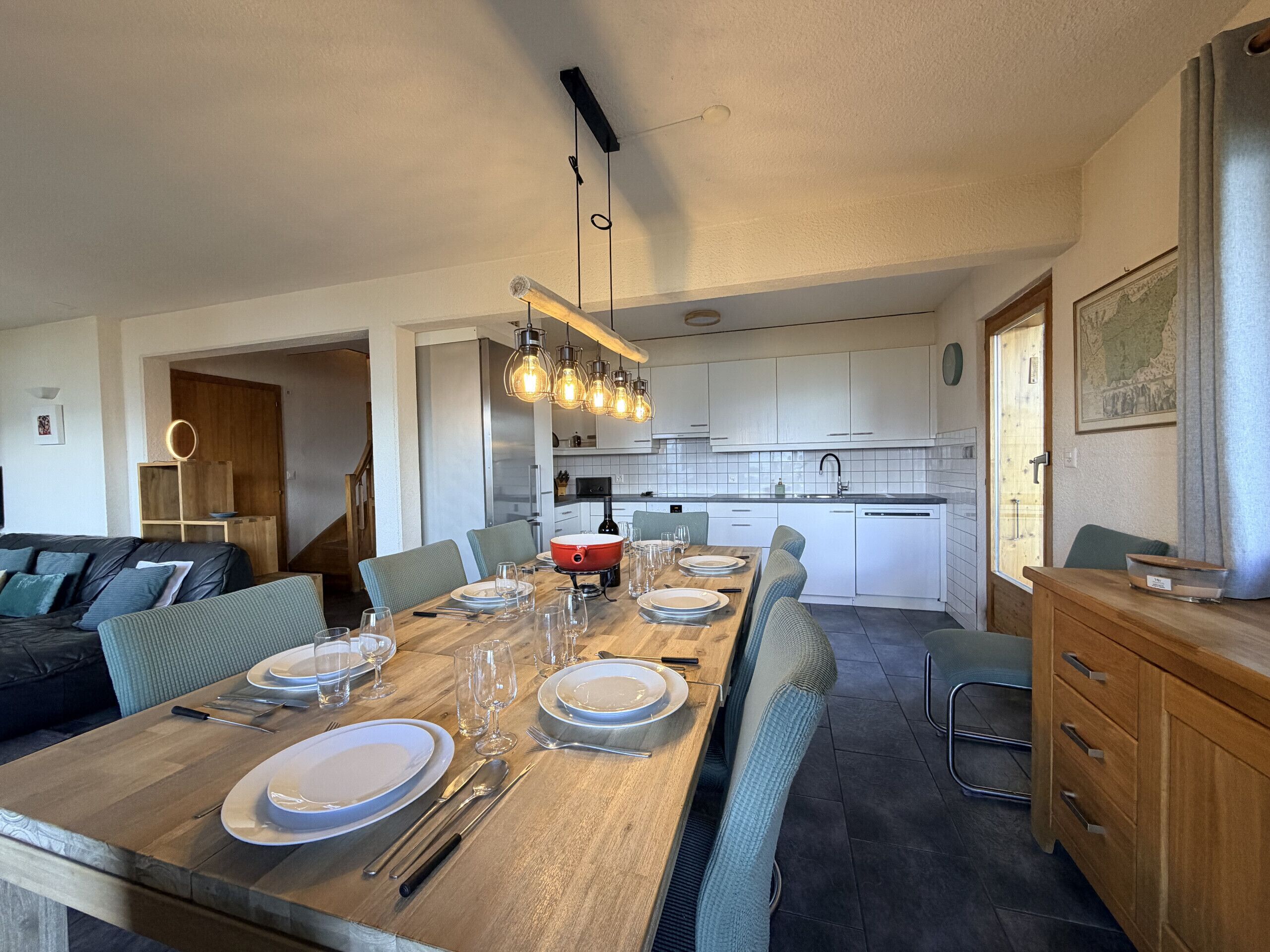 Een moderne keuken met witte kasten, een houten eettafel gedekt voor zes personen, en een trap die naar een hoger niveau leidt.