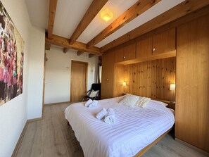 A bedroom with a large bed, wooden panel walls, a chair, and a painting on the wall.