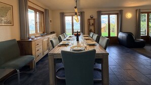 Un espace repas comprenant une longue table, des chaises, un lustre et une vue sur l’extérieur.