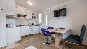 Een kleine keuken met witte kastjes, een magnetron, waterkoker en broodrooster. Er is een eethoek met een tafel en twee stoelen.
