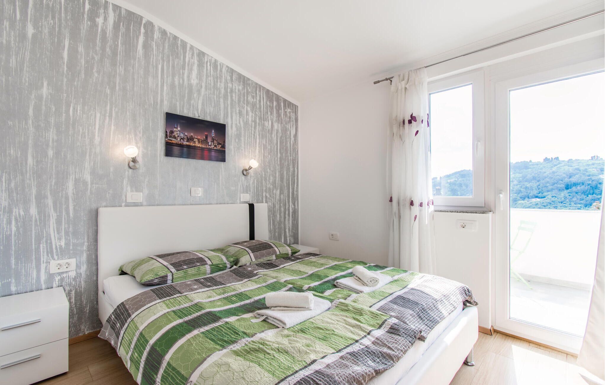 Ett sovrum med en säng, en tavla med en stadsbild på väggen och utsikt över en kulle genom ett fönster.