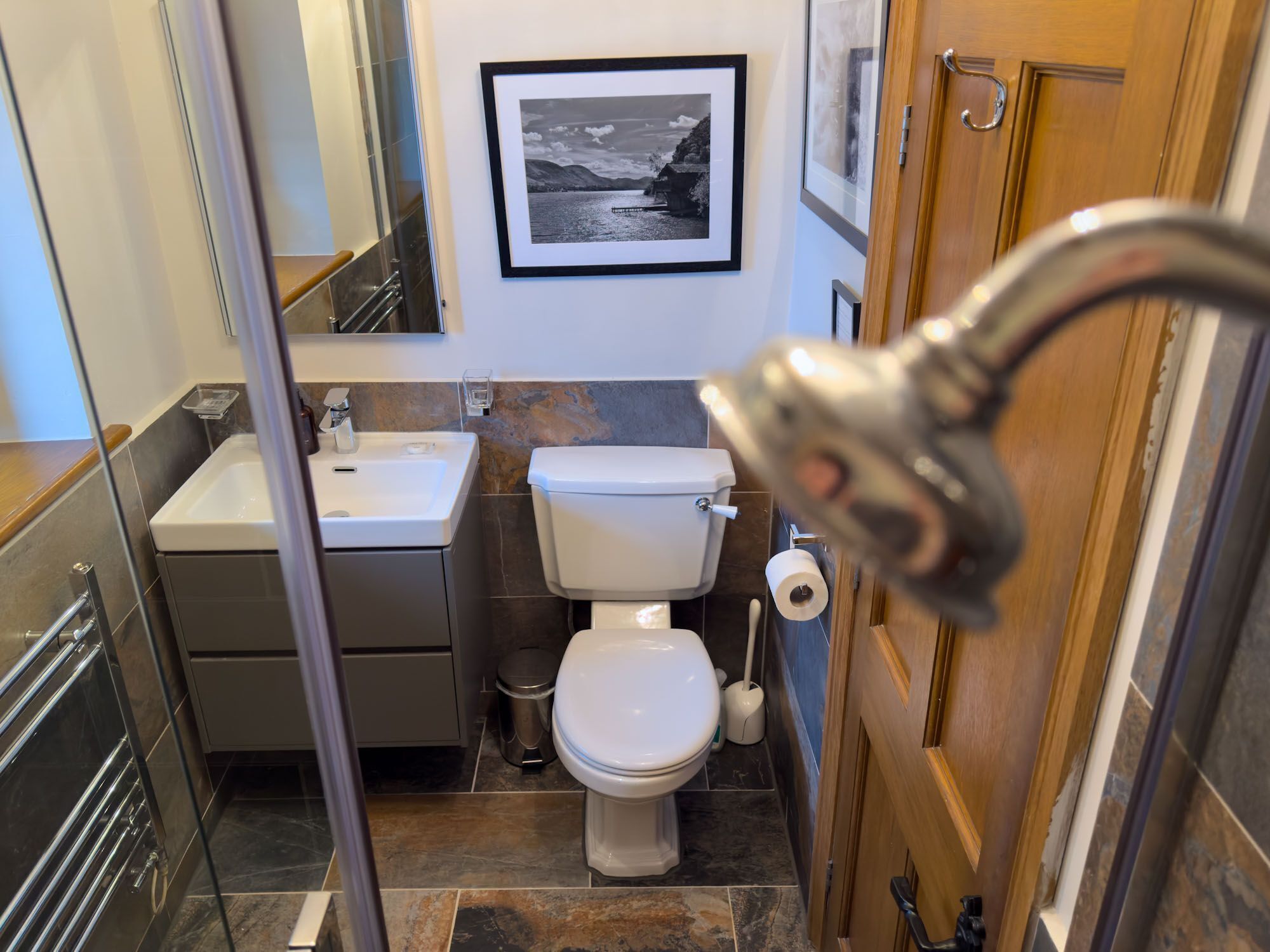 A compact bathroom with a sink, toilet, and shower. A framed photograph is on the wall.