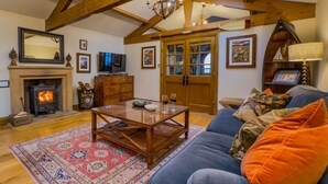 A cozy living room with a fireplace, wooden beams, a sofa, and a coffee table. - Luxury, romantic boathouse on the shores of Lake Ullswater, perfect for special occasions. (Ullswater)