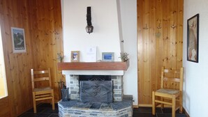 Ein Zimmer mit Kamin aus Stein, Holzstühlen, einer Holzwand mit Haken und einem gerahmten Bild an der Wand.