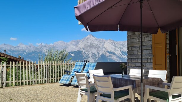 A patio with a table and chairs, a purple umbrella, and a mountain view. - Greppons P 003 - MOUNTAIN apartment 7 pers (Veysonnaz)