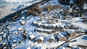A snow-covered mountain village with chalet-style buildings, winding roads, and a backdrop of snow-capped peaks. - Greppons P 003 - MOUNTAIN apartment 7 pers (Veysonnaz)