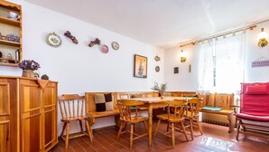 Uma área de refeições com mobiliário de madeira, piso de azulejos e decorações nas paredes, incluindo pratos e uma imagem emoldurada.