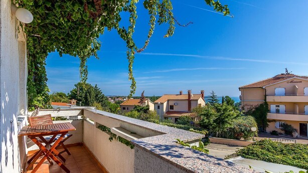 A balcony with a wooden table and chairs, overlooking a residential area with houses and a clear blue sky. - Large apartment with air conditioning, WiFi (Premantura)