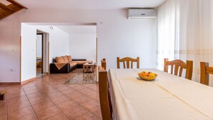 A modern living room with a dining table set for four, a sofa, and a kitchen area in the background. - Large apartment with air conditioning, WiFi (Premantura)