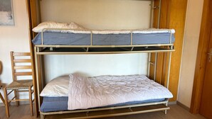 Un lit superposé à deux niveaux, une chaise en bois et une porte à l’arrière-plan.