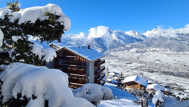 Un village de montagne enneigé, avec des bâtiments en bois et un ciel d’un bleu limpide.