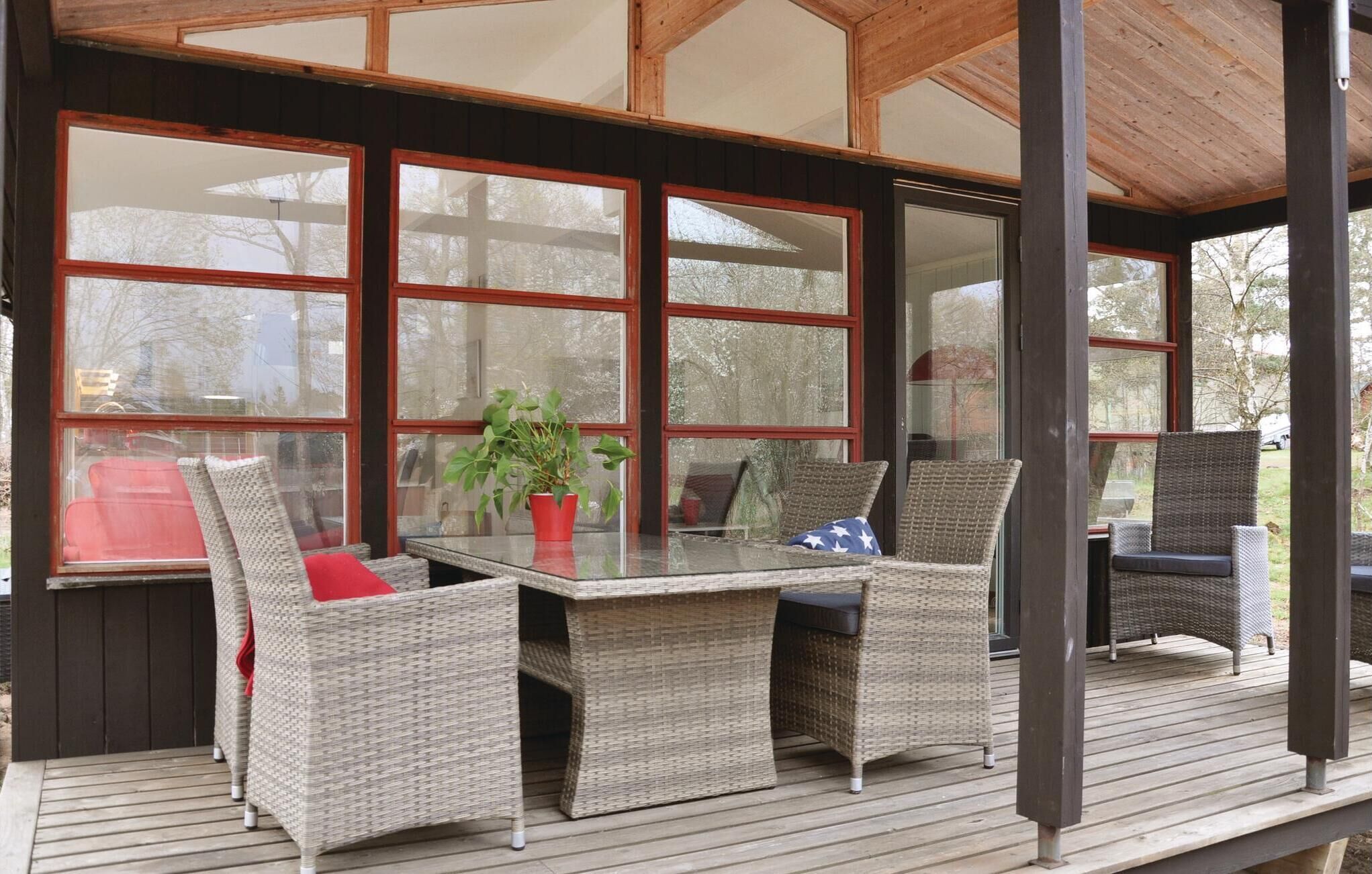 A covered outdoor seating area with wicker furniture, large windows, and a wooden deck.