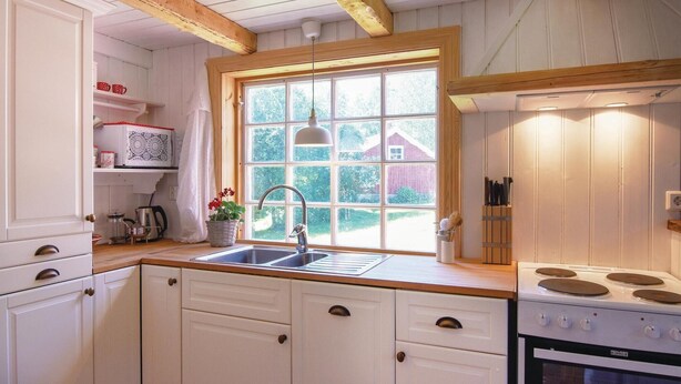 A kitchen with white cabinets, a window with a view of a red barn, a sink, and a stove.