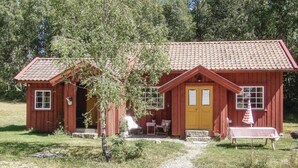 A red wooden cabin with a tiled roof, a small porch, and a table with a checkered tablecloth outside.