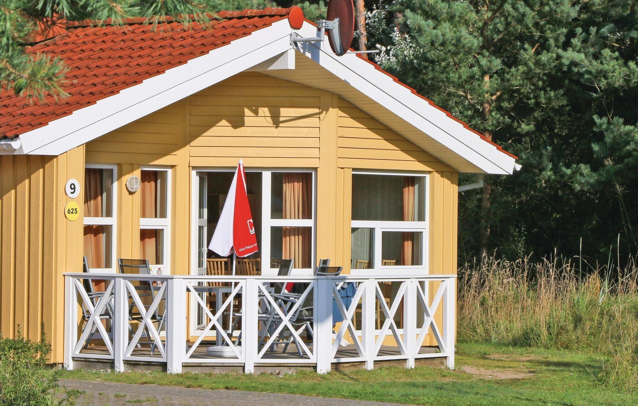 A yellow building with a red roof, white windows, and a white porch with a red and white umbrella.