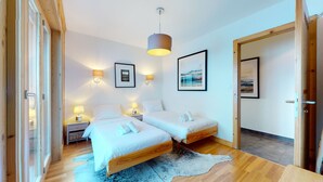 Une chambre moderne avec deux lits, un plancher en bois, un grand tapis et des lampes fixées au mur.