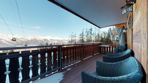 Une terrasse en bois avec des chaises en osier, une balustrade en bois et une vue sur des montagnes enneigées.