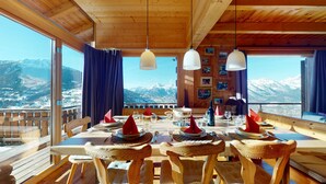 Ein Esszimmer mit Holzboden, einem Tisch für sechs Personen, großen Fenstern mit Blick auf die Berge und hängenden Pendelleuchten.