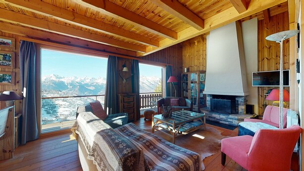 Ein gemütliches Zimmer mit großem Fenster, Holzbalken, Kamin und einer bequemen Sitzecke.