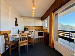Una cocina compacta con muebles blancos, estufa y comedor con sillas y mesa de madera.