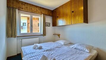 Une chambre d’hôtel avec un grand lit, des lambris en bois sur les murs, une fenêtre avec des rideaux et une petite étagère.