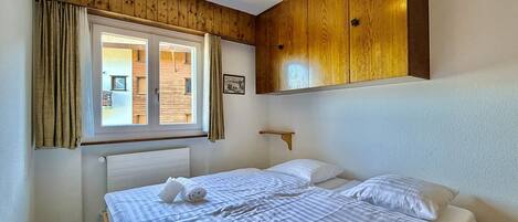 Una habitación de hotel con una cama grande, paneles de madera en las paredes, una ventana con cortinas y una pequeña estantería.