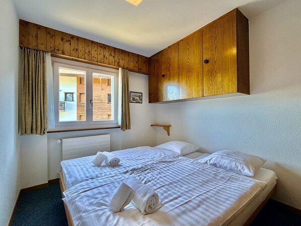 Una habitación de hotel con una cama grande, paneles de madera en las paredes, una ventana con cortinas y una pequeña estantería.