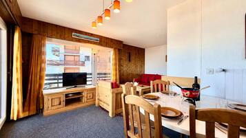 Une pièce chaleureuse avec un décor intérieur en bois, une télévision, une table à manger avec des chaises et un canapé rouge.