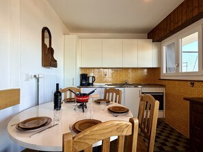 Un comedor con una mesa redonda dispuesta para cuatro, una cocina al fondo y una ventana con vistas.