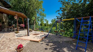A playground with a swing set and climbing structure, surrounded by trees and a stone patio. - Beautiful home in Plaski (Plaski)