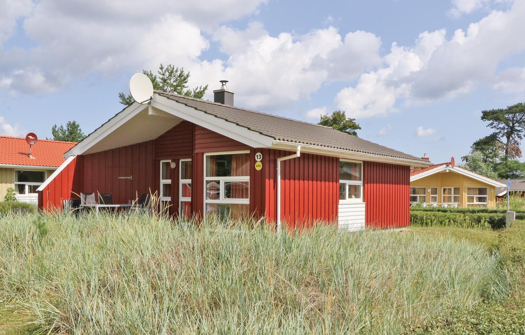 A red building with a white door and windows, surrounded by tall grass.