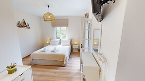 Une chambre d’hôtel avec un lit, des lampes de chevet, un téléviseur fixé au mur et une fenêtre donnant sur un paysage verdoyant.