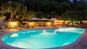 Une piscine entourée de murs de pierre et d’arbres, avec des chaises longues et des parasols.