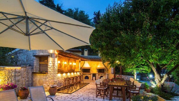 Une terrasse extérieure avec un sol en pierre, des meubles en bois et un coin bar agrémenté de jeux de lumière.