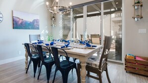 Uma sala de jantar com uma mesa grande posta para seis pessoas, rodeada de cadeiras e um lustre acima.
