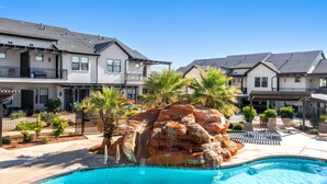 Uma área residencial com piscina, cachoeira artificial em rocha e casas com varandas e espaços para estar ao ar livre.