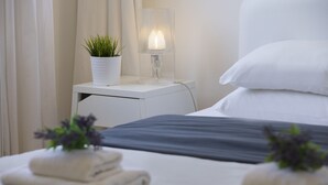 A neatly made bed with pillows, a bedside table with a lamp, and a potted plant.
