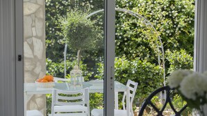 A glass table with white chairs, a stone wall, and a garden with various plants and a birdcage.