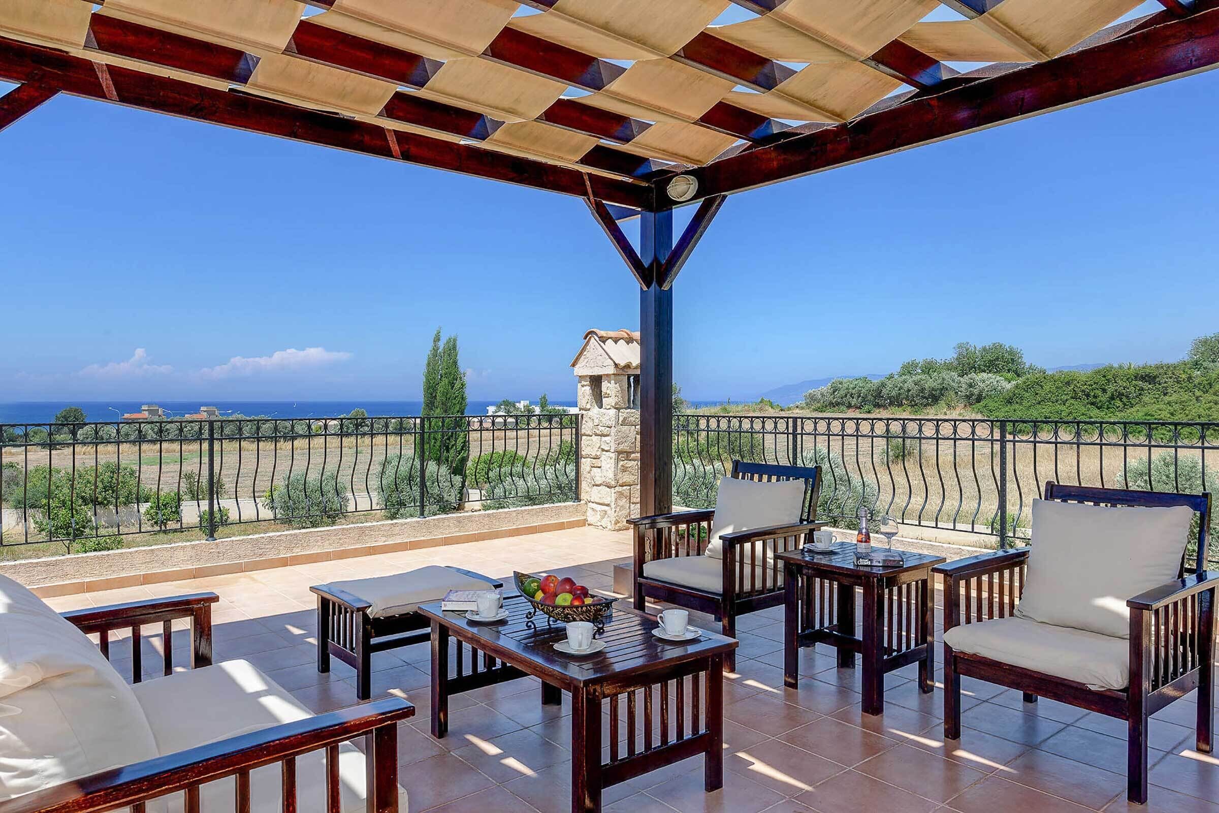 Un espace extérieur abrité, aménagé avec des chaises et des tables en bois, offrant une vue sur la mer, et dont l’arrière-plan est constitué d’une structure en pierre.