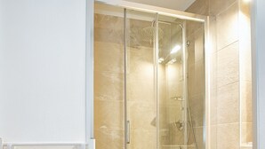 Un baño moderno con ducha envuelta en cristal, tocador blanco con cajones y un perchero para toallas.