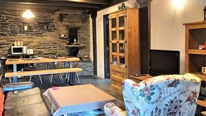 A cozy living area with stone walls, a wooden cabinet, and a floral-patterned armchair. - The Balcony of Sotillo. Near Las Médulas (Sotillo de Cabrera)