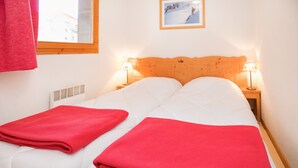 Ein Doppelbett mit zwei roten Decken, ein hölzerner Kopfteil, zwei Nachttischlampen, ein Fenster mit Blick auf Gebäude und ein gerahmtes Bild an der Wand.
