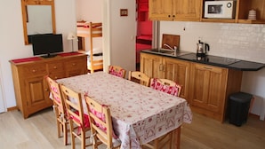 Cocina compacta con armarios de madera, un microondas y una mesa de comedor con sillas.