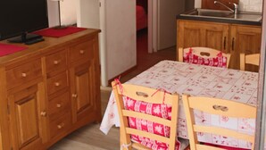 Cocina compacta con armarios de madera, una mesa de comedor con sillas y un televisor sobre un aparador de madera.