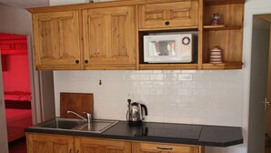Una cocina con armarios de madera, encimera negra, microondas y hervidor.